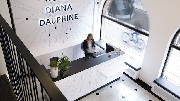 Una recepción de hotel con diseño moderno, una recepcionista y vistas a la calle.