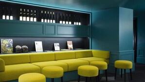 Una zona de bar color turquesa con un sofá amarillo y taburetes a juego, una vinoteca encima y cuadros en la pared.
