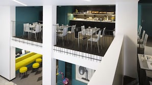 Un interior moderno, de varios niveles, con zona de comedor en la parte superior, área de cocina en la inferior y un espacio de descanso con taburetes amarillos.