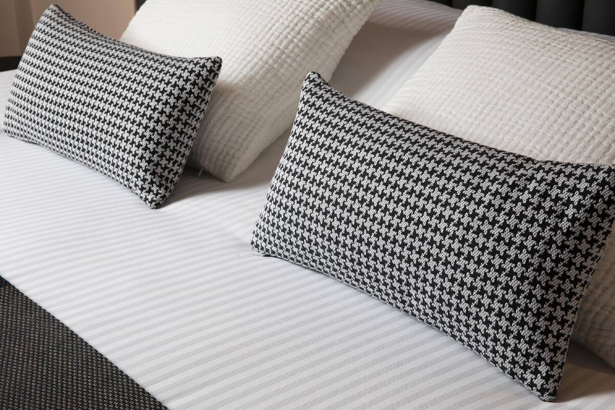 A bed with white bedding and two black and white patterned pillows.