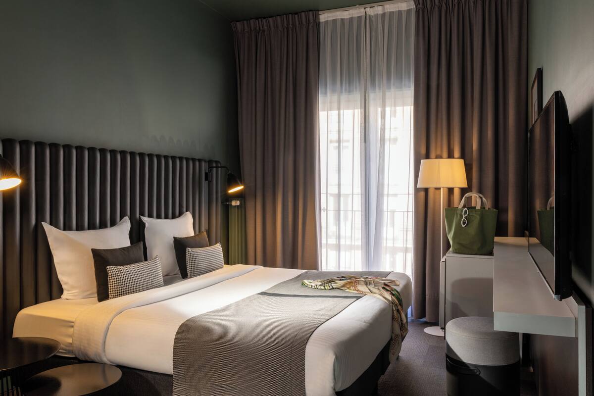 A hotel room with a bed, bedside lamps, a desk with a lamp, a chair, and a TV.
