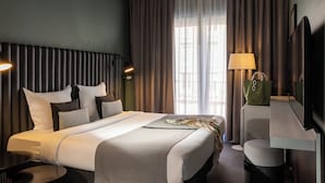 Una habitación de hotel con una cama, lámparas de noche, un escritorio con lámpara, una silla y un televisor.