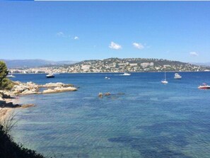 A coastal view with clear blue water, rocky shore, and boats. - Hotel Festival (Cannes)