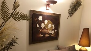 A living room with a brown sofa, a framed painting of flowers, a lamp, and decorative plants. - Hotel Festival (Cannes)