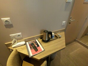 Quarto de hotel com escrivaninha de madeira, controle remoto, cafeteira e uma revista.