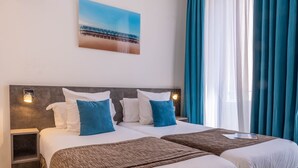 A double bed with white and blue pillows, a brown bedspread, and a nightstand with a lamp. - Hotel de la Fontaine (Nice)
