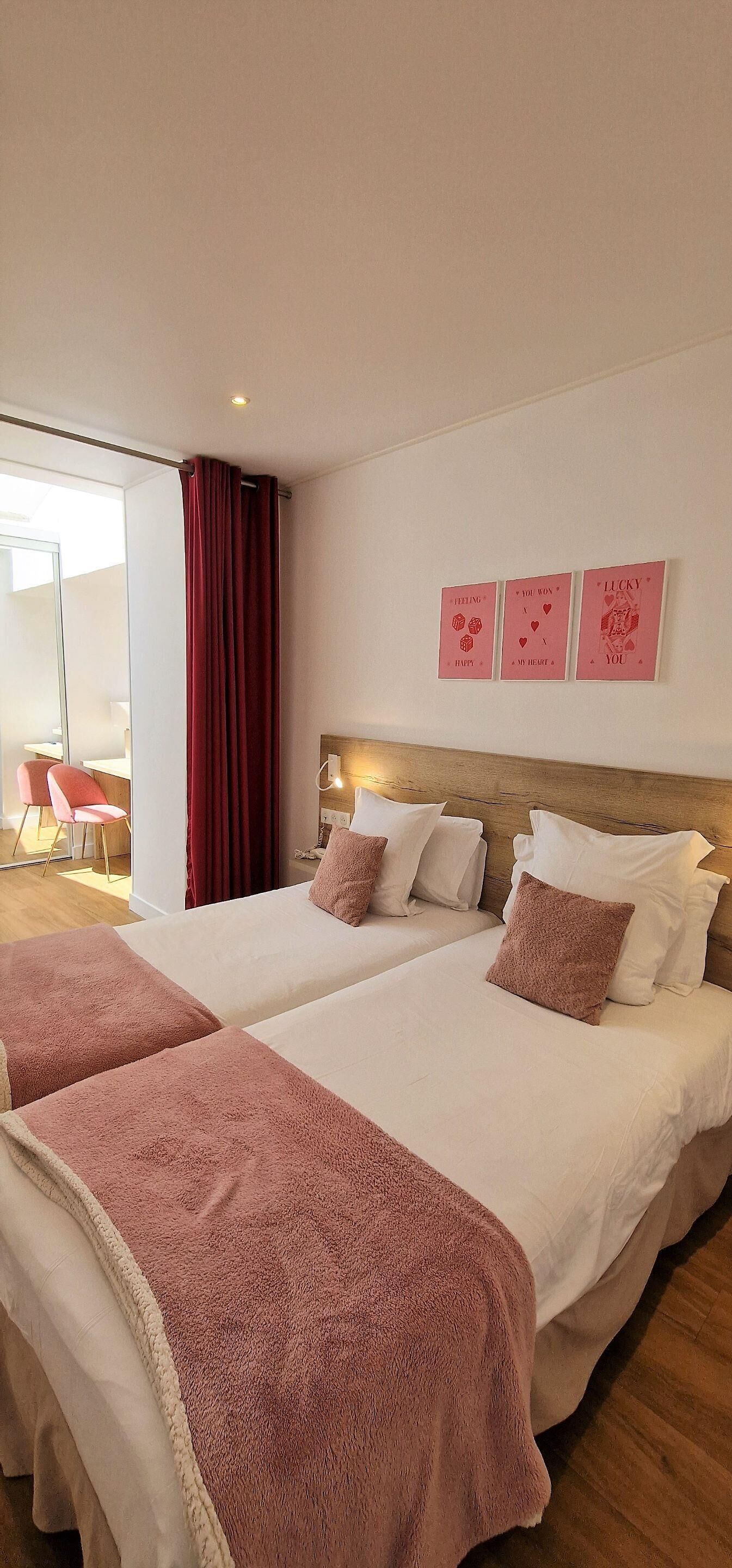 Ein Hotelzimmer mit zwei Betten, einem Holzkopfstück und einem großen Fenster mit roten Vorhängen.