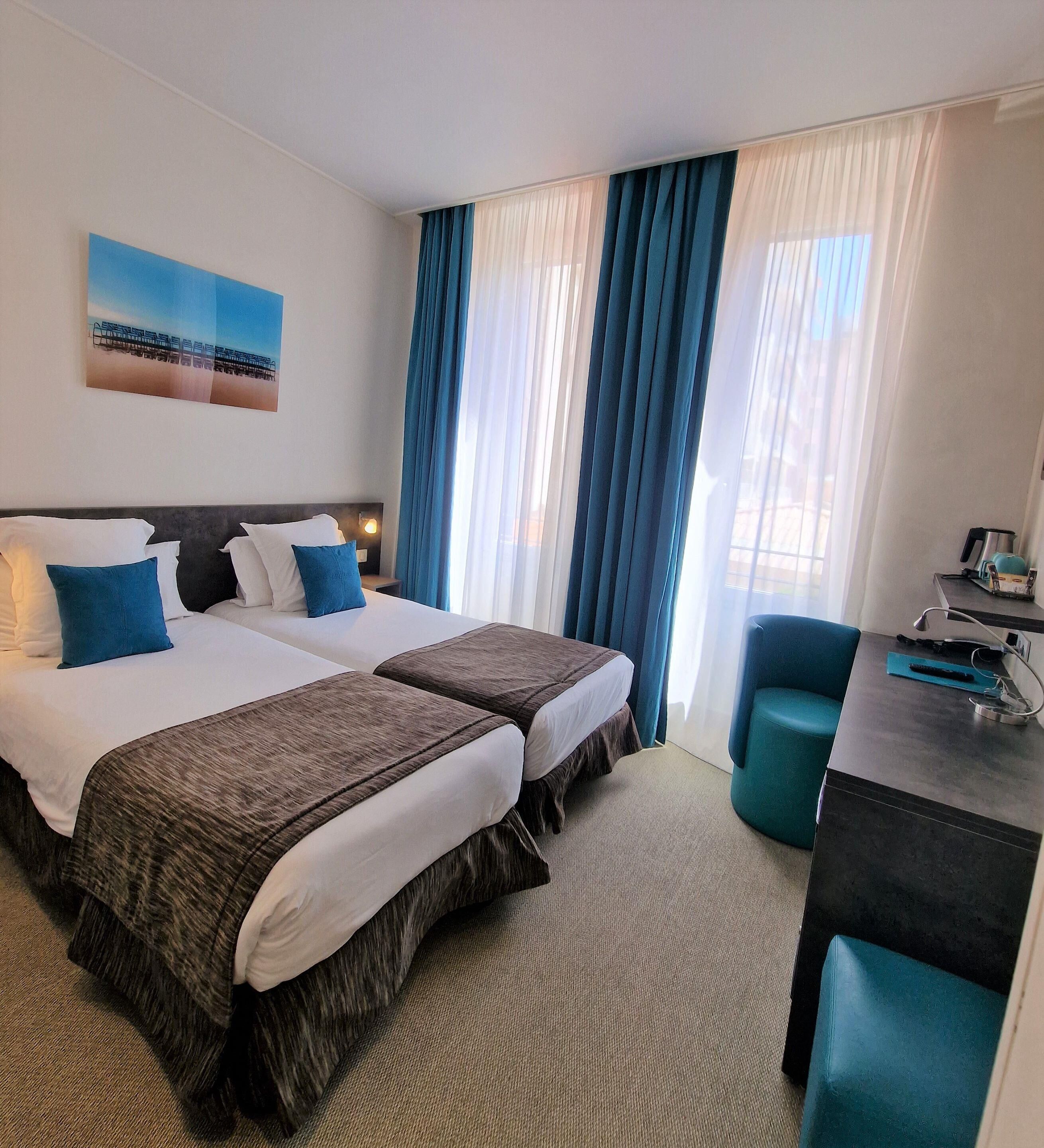 Habitación de hotel con dos camas, un escritorio, una silla y vista al exterior.