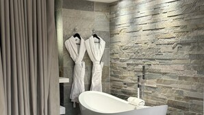 Un baño moderno con una bañera independiente, salpicadero de pared de piedra y dos toallas blancas colgadas de ganchos.