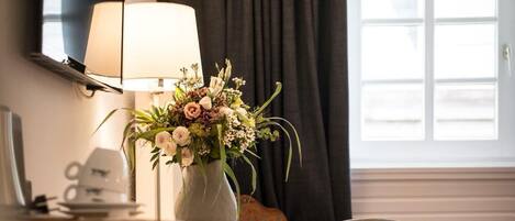 A room with a wooden desk, a chair, a lamp, and a vase with flowers.