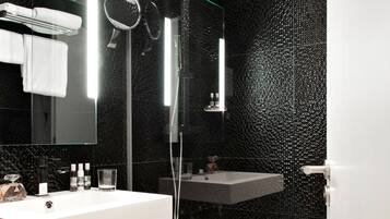 A modern bathroom with a large mirror, two sinks, a shower, and a toilet.