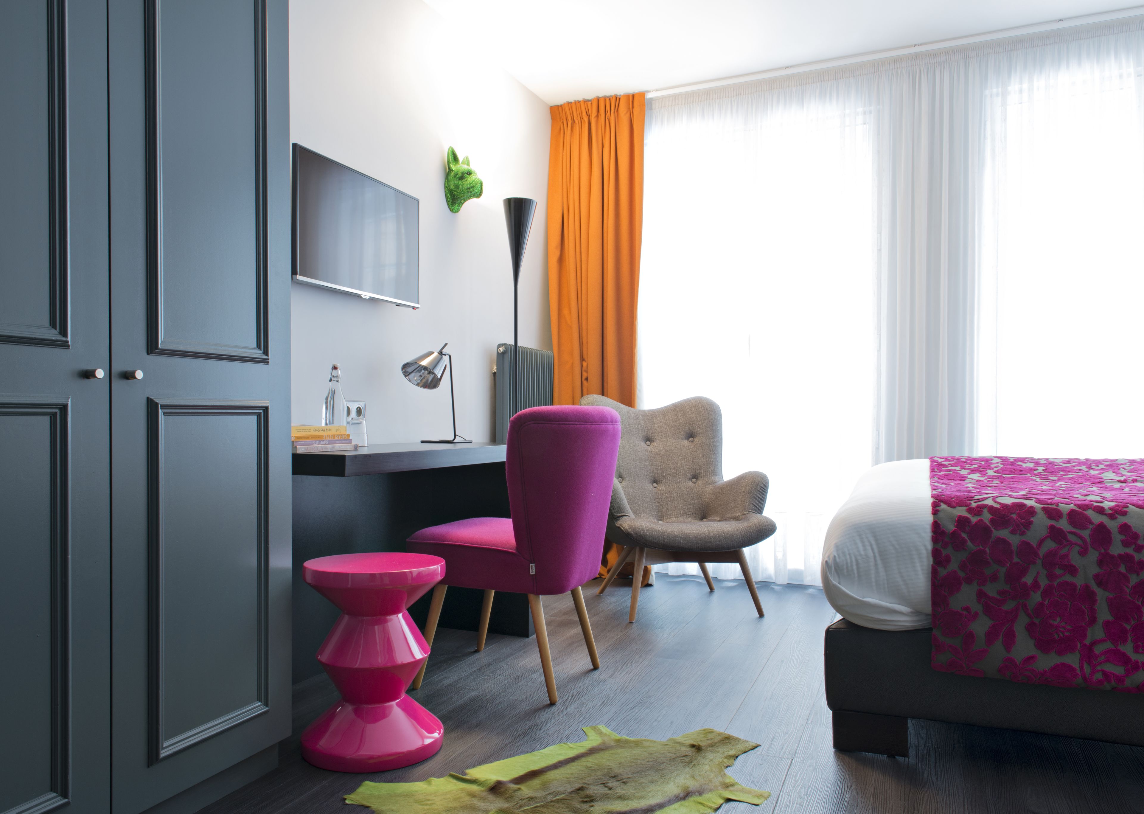 Une chambre d’hôtel moderne équipée d’un bureau, d’une chaise, d’un lit et d’une grande fenêtre avec des rideaux.