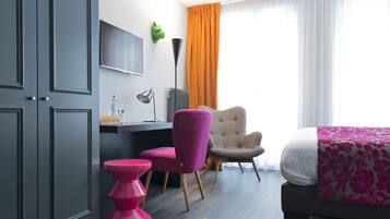Une chambre d’hôtel moderne équipée d’un bureau, d’une chaise, d’un lit et d’une grande fenêtre avec des rideaux.