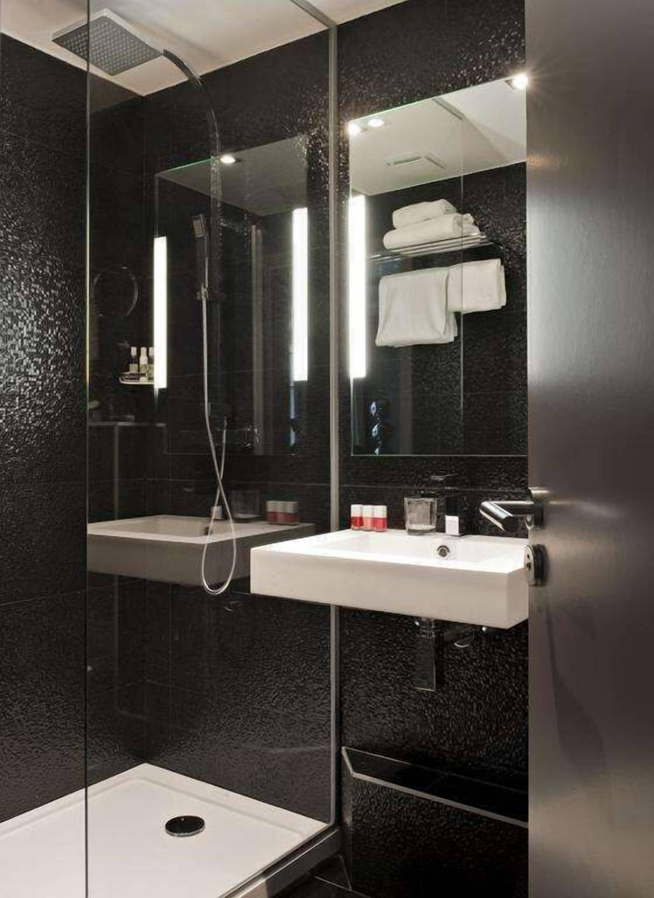 Un baño moderno con ducha envuelta en vidrio, un lavabo blanco y un espejo grande.