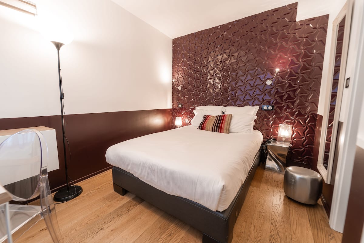 A modern hotel room with a large bed, a desk, and a unique geometric wall design.