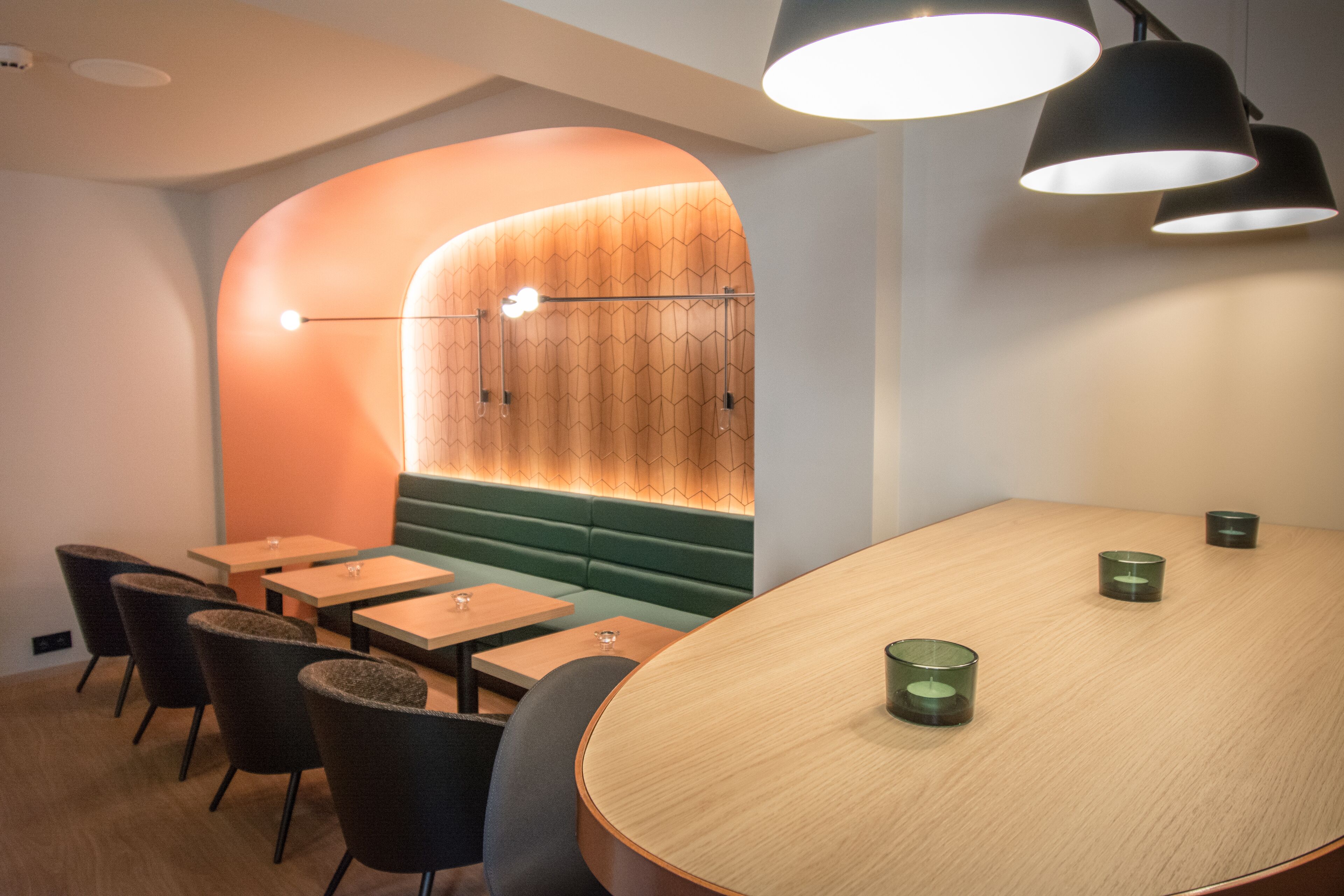 Un interior moderno con una mesa de madera, asientos acolchados de color verde e iluminación colgante.