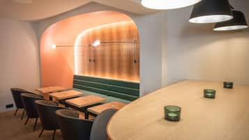 Un interior moderno con una mesa de madera, asientos acolchados de color verde e iluminación colgante.