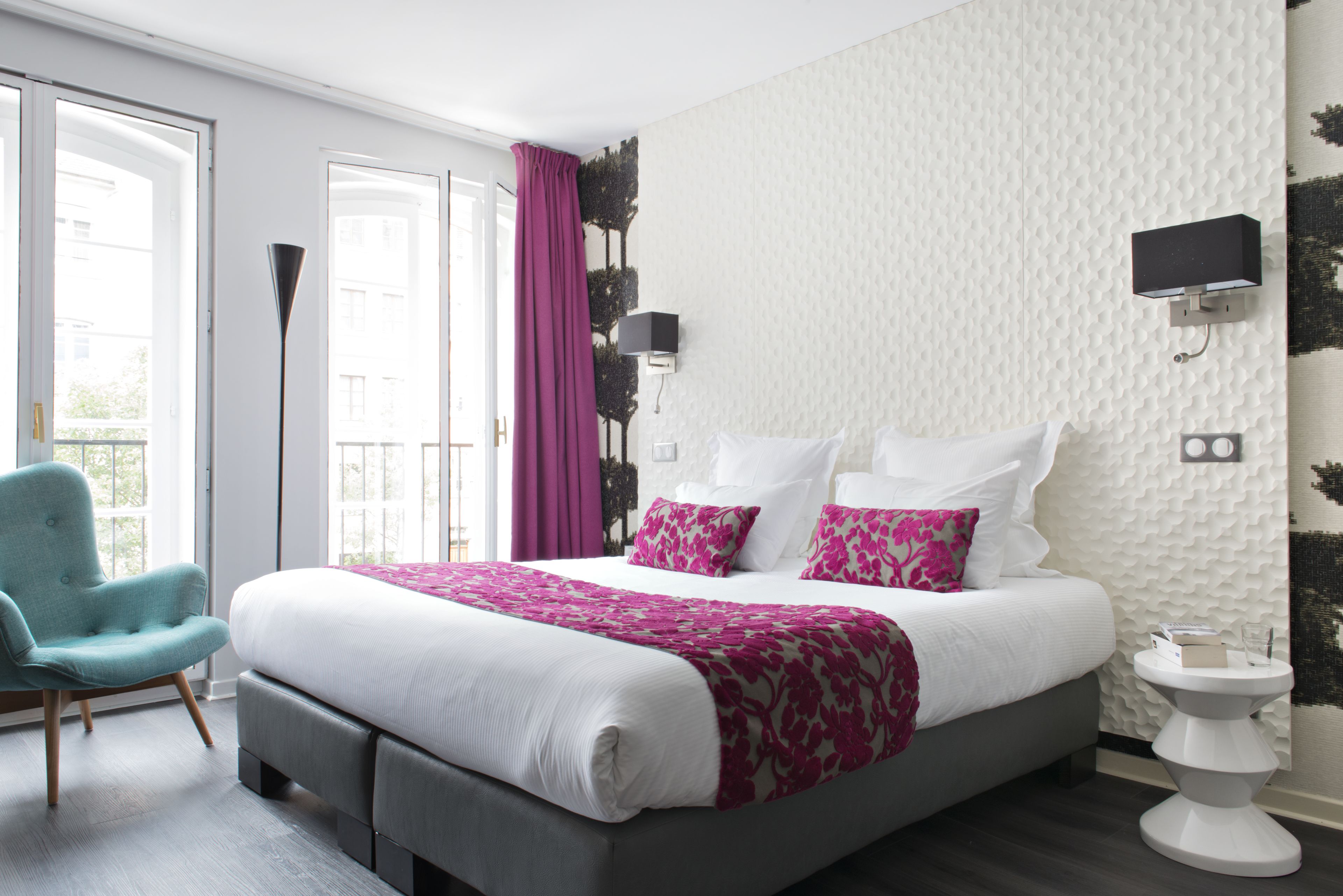 Une chambre moderne avec un grand lit, un fauteuil, une table de chevet et un téléviseur fixé au mur.