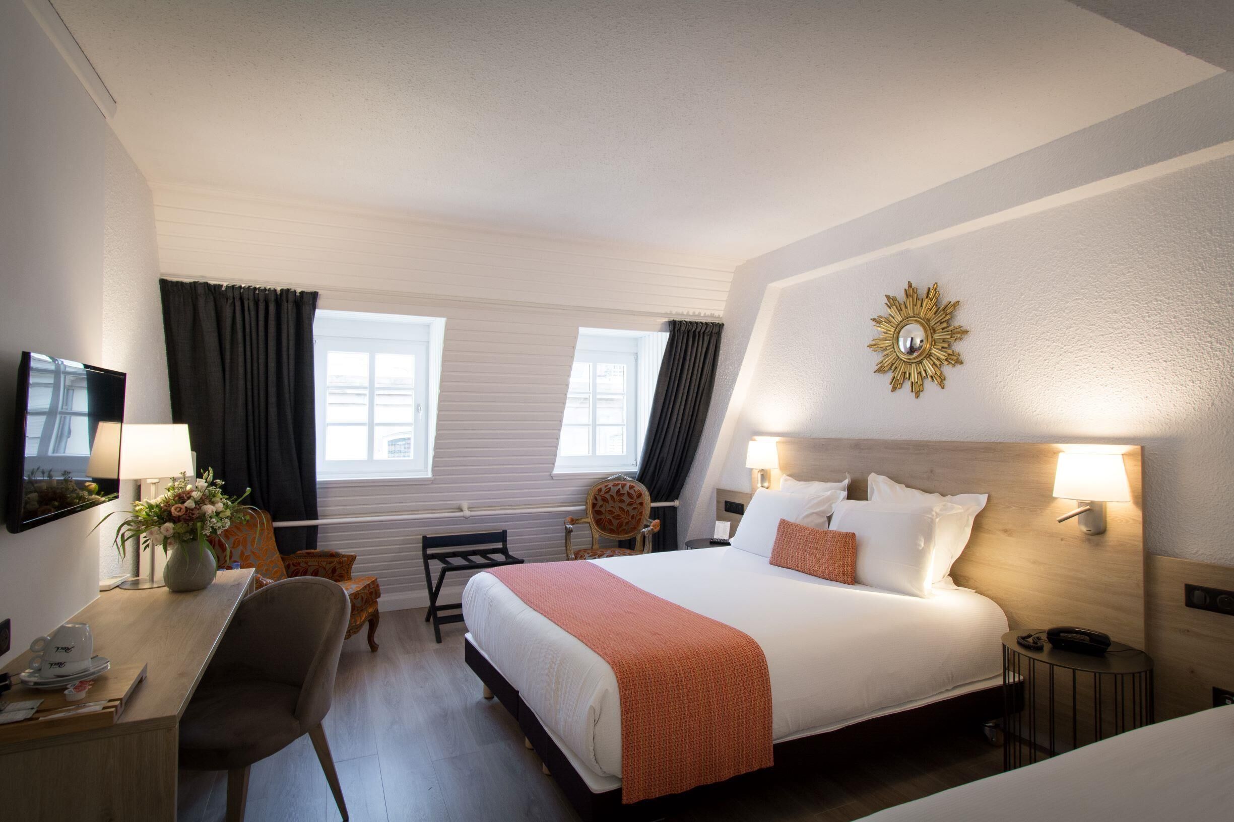 A hotel room with a bed, bedside tables, a desk, a chair, and a TV.