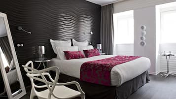 A modern hotel room with a large bed, a white chair, a mirror, and a bedside table.