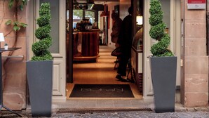 Fachada clásica de un hotel, entrada acogedora y zona interior visible con un bar.