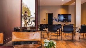A modern hotel lobby with leather seating, a flat-screen TV, and a view of the street outside. - L'Hôtel - Face au Château - Boutique Hôtel et Séminaires (Nantes)