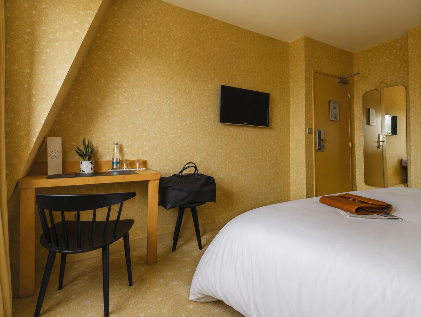 Una habitación de hotel con una cama, un escritorio con una silla, un televisor y un espejo.