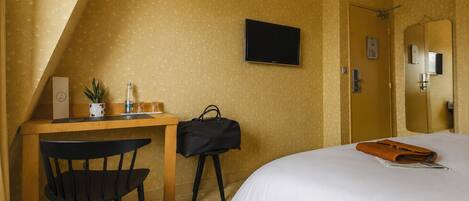 Una habitación de hotel con una cama, un escritorio con una silla, un televisor y un espejo.