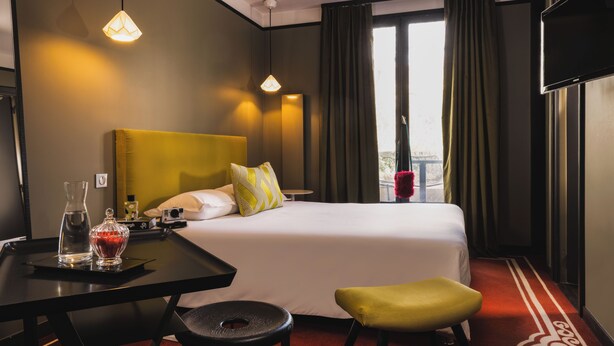 A hotel room with a bed, a desk with a chair, a window with curtains, and a television. - L'Hôtel - Face au Château - Boutique Hôtel et Séminaires (Nantes)