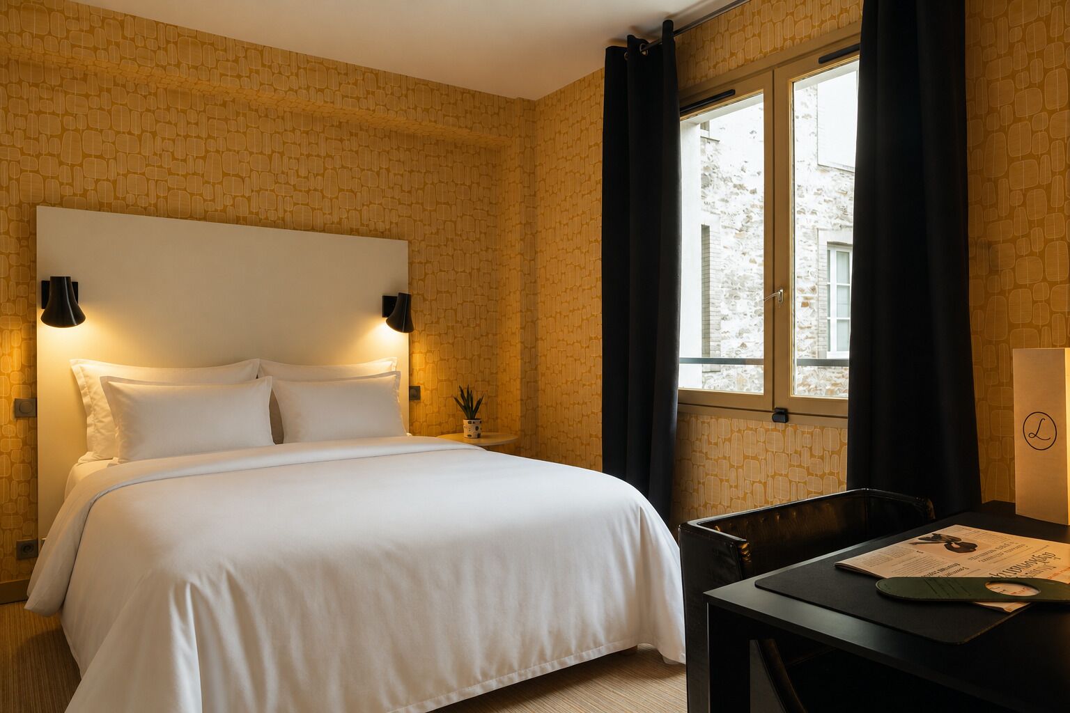 Una habitación de hotel con cama, escritorio, lámpara y ventana con cortinas.