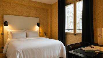 Una habitación de hotel con cama, escritorio, lámpara y ventana con cortinas.