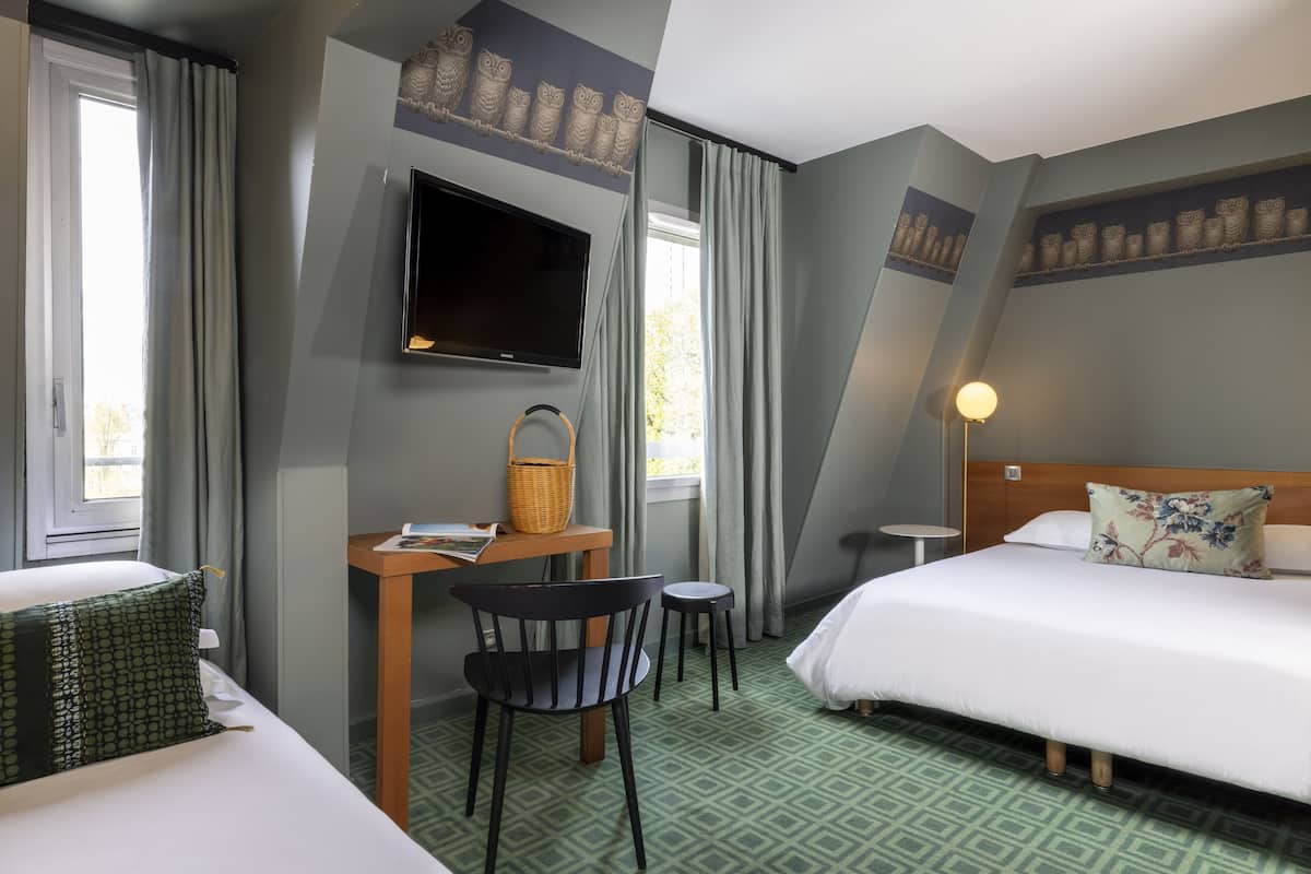 Ein Hotelzimmer mit einem Bett, einem Schreibtisch mit Stuhl, einem Fernseher und einem Fenster mit Vorhängen.