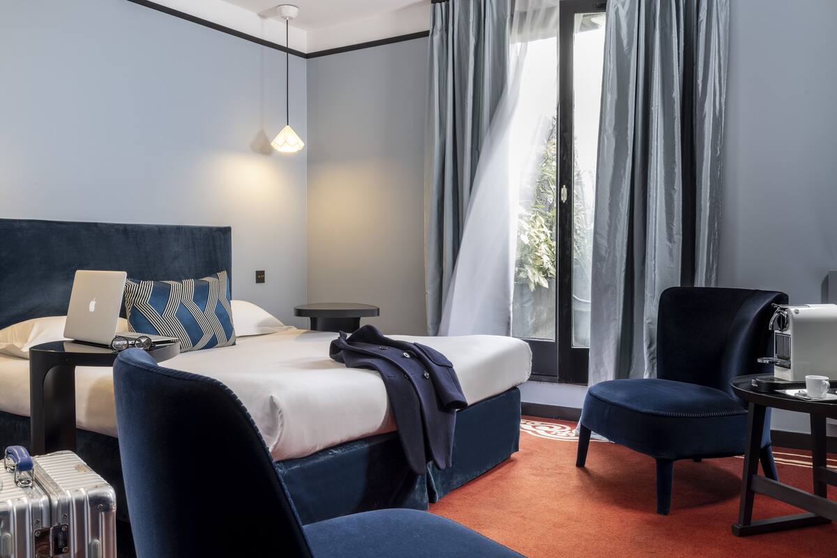 Ein Hotelzimmer mit einem Bett, einem Schreibtisch, einem Stuhl, einem Koffer und einem Fenster mit Vorhängen.