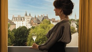 A person standing by a window overlooking a historic building complex with multiple towers and spires. - L'Hôtel - Face au Château - Boutique Hôtel et Séminaires (Nantes)
