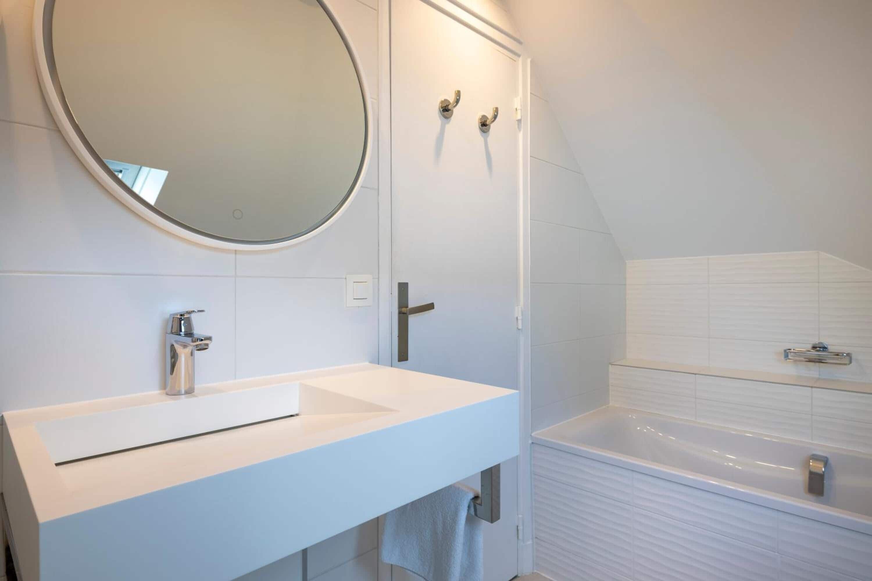 Un baño moderno con un lavabo blanco, un espejo redondo y una bañera.
