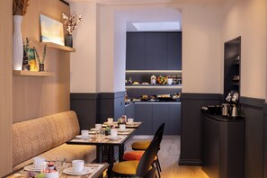 A modern dining area with a sofa, dining table, and chairs. A kitchen is visible in the background. - Le 46 Hotel (Paris)