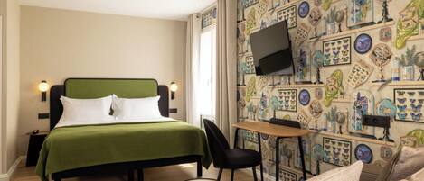 A hotel room with a bed, a desk, a TV, and a patterned wall.