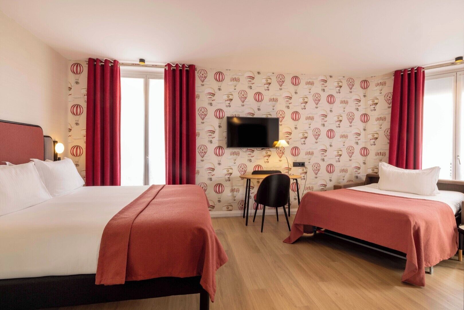 Une chambre d’hôtel avec deux lits, un bureau, une télévision et une fenêtre avec des rideaux.