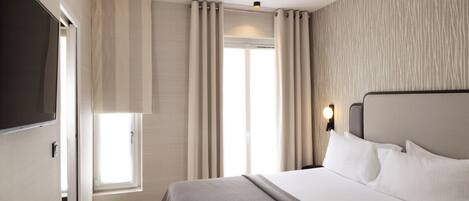 Una habitación de hotel moderna con una cama grande, un televisor de pantalla plana, una ventana con cortinas y una lámpara fijada a la pared.