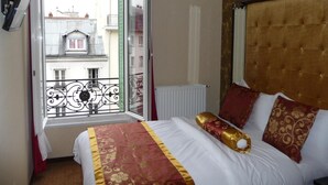 Habitación de hotel con cama, ventana que ofrece vistas a edificios, radiador y pared con un diseño texturizado.