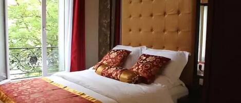 A bedroom with a large window, a tufted headboard, and a patterned bedspread.