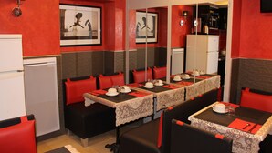 Un restaurante con decoración roja y negra, varias mesas dispuestas para comer y una zona de cocina visible a través de una partición.