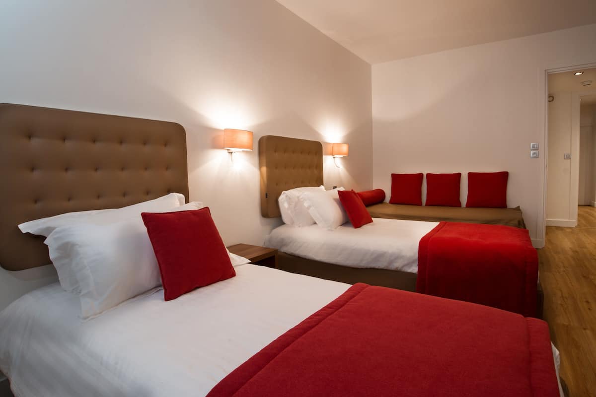 Ein Hotelzimmer mit zwei Betten, jeweils mit Kopfteil, weißer Bettwäsche und roten Akzenten.