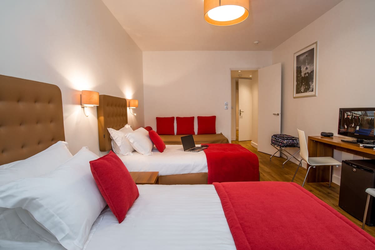 Ein Hotelzimmer mit zwei Betten, einem Schreibtisch, einem Sessel und einem Fernseher.