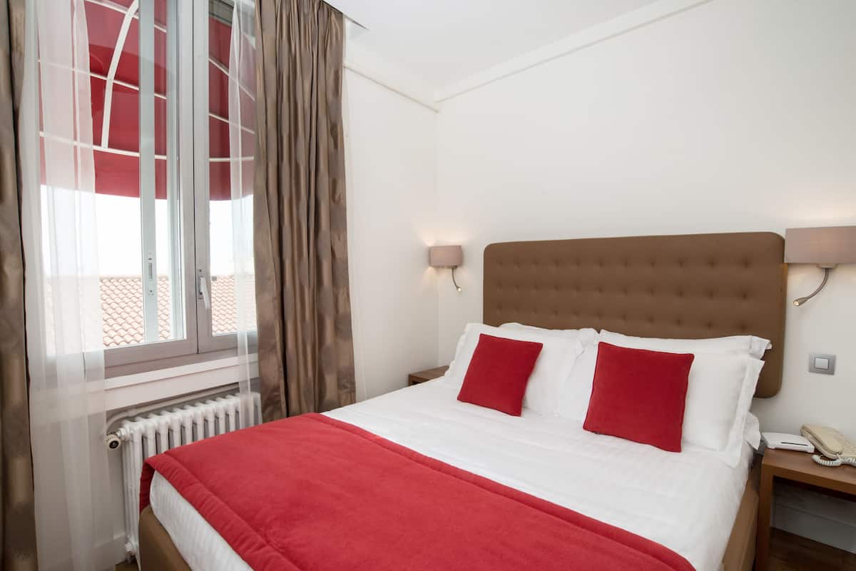 Ein Hotelzimmer mit einem Bett, einem Nachttisch, einer Lampe und einem Fenster mit Vorhängen.