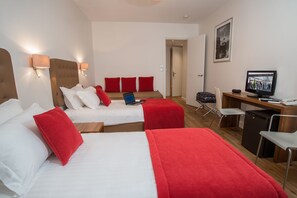 A hotel room with two beds, a desk, a television, and a small refrigerator. - Hotel De France (Cannes)