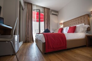 Habitación de hotel con cama, escritorio, silla y ventana con cortinas.