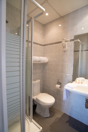 Un baño moderno con cabina de ducha de vidrio, inodoro, lavabo con artículos de aseo y espejo.