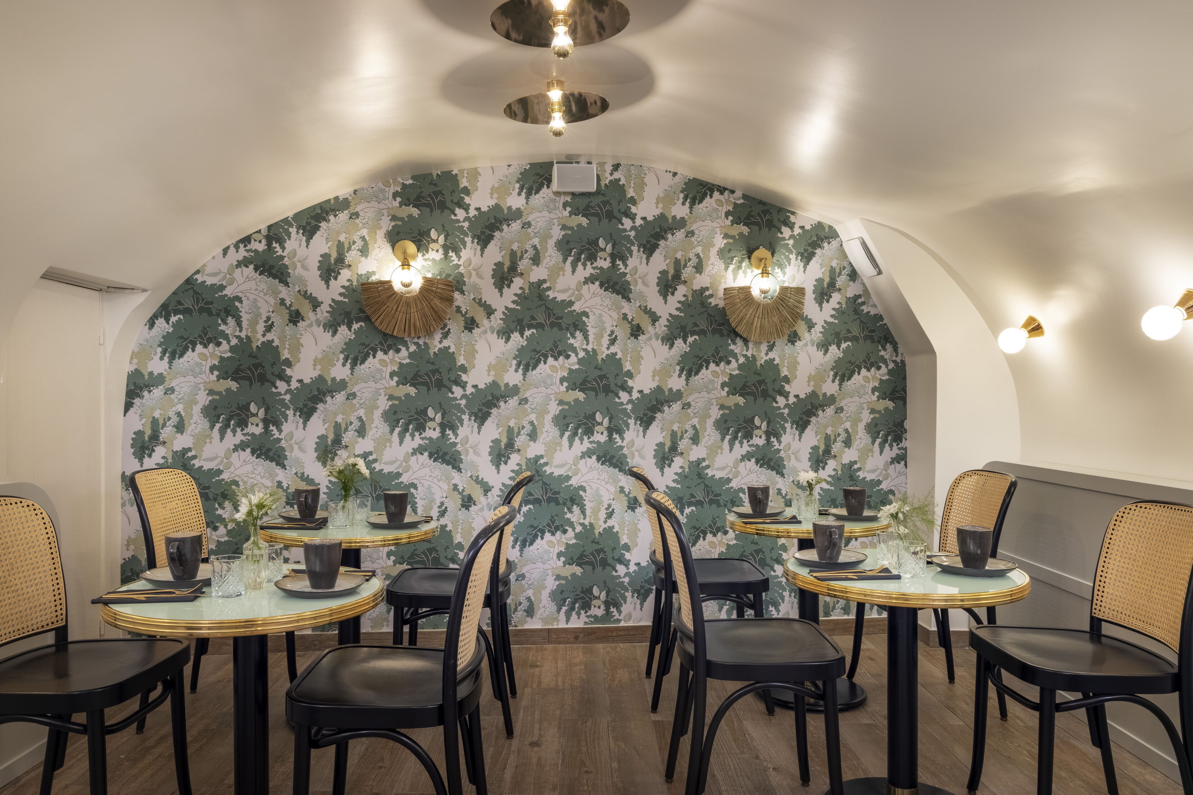 Een eethoek met ronde tafels, zwarte stoelen en een muur met een bladpatroon.