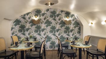 Een eethoek met ronde tafels, zwarte stoelen en een muur met een bladpatroon.